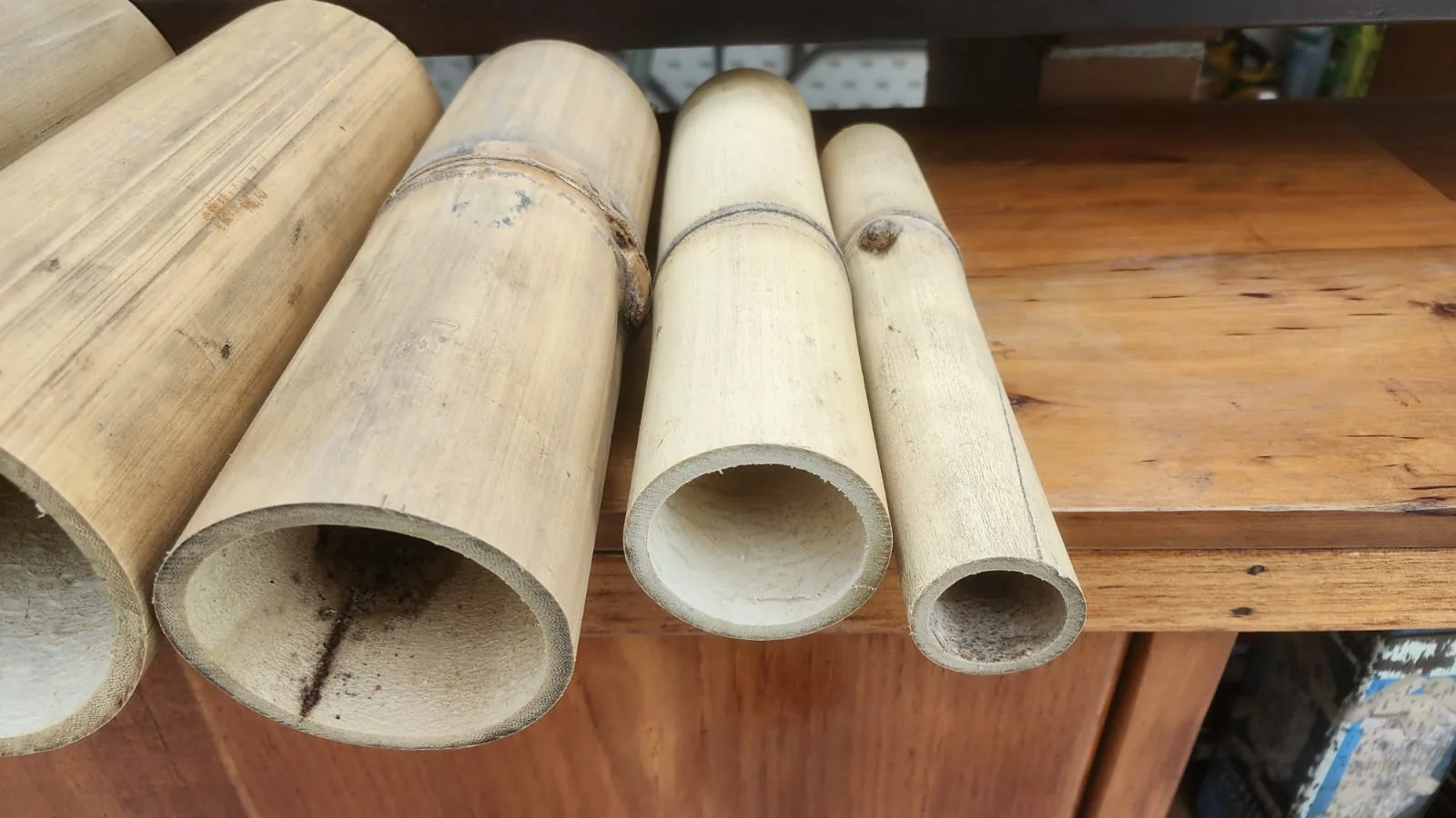 Cuatro cañas de bambú cortadas y alineadas sobre una mesa de madera, de mayor a menor diámetro, con el corte a la vista mostrando el interior hueco y el grosor de la pared.